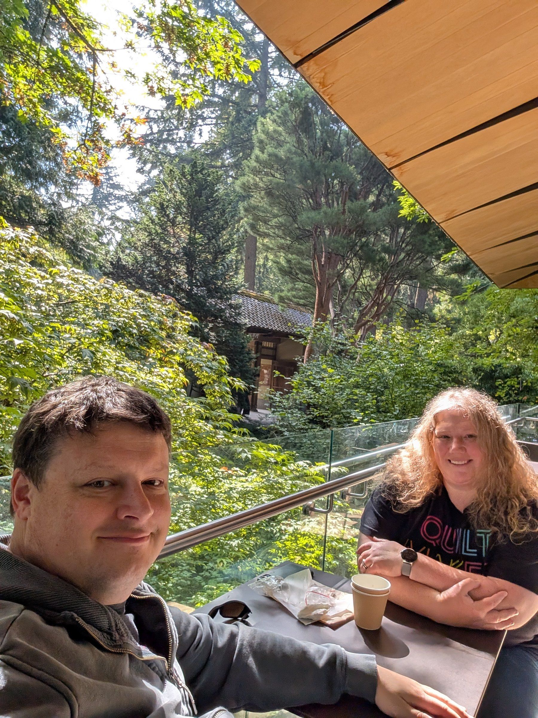 The two of us at a table with a cup of tea, on a terrace
    overlooking the trees of the garden.